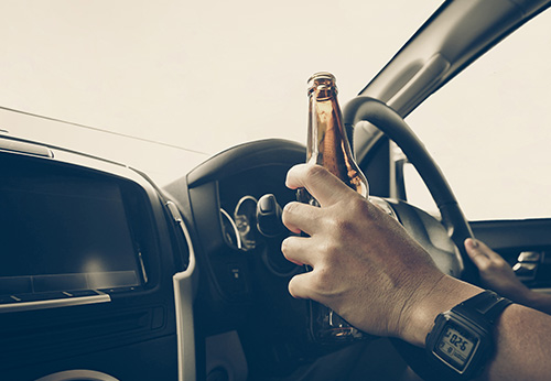 Close-up of a person holding a beer bottle while driving, illustrating the consequences of DUI convictions in Pasadena, CA